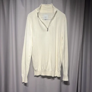 Vit stickad half zip-tröja från Erla - Snygg vit stickad tröja från Erla of Sweden med half zip-dragkedja i halsen. Tröjan har långärmade ribbade muddar och en stilren, klassisk look. Perfekt för dig som gillar enkel och clean stil med lite extra detaljer. Nypris 1000kr
