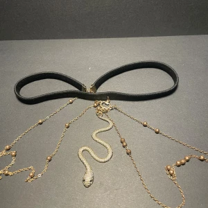 Smycken för låret  - Cool svart smycke för låret med en hängande guldorm i metall och tunna guldfärgade kedjor med små pärlor. Ormen har detaljerad struktur och ger ett edgy och unikt intryck. Perfekt för dig som vill sticka ut med ditt smycke.
