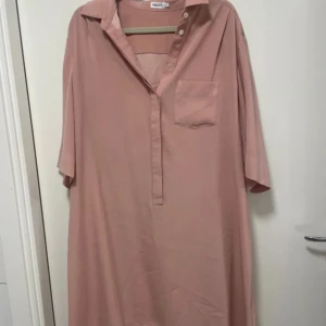 Rosa skjortklänning från Filippa K - Ljusrosa skjortklänning från Filippa K med avslappnad passform, trekvartsärm och klassisk krage. Klänningen har knappar framtill och en bröstficka. Tillverkad i mjukt och lätt material som ger en skön känsla.