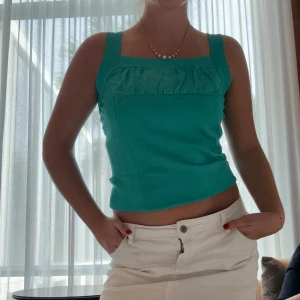 Turkos linnetopp med volangdetalj - Snygg turkos linnetopp med breda axelband och volangdetalj framtill. Toppen har en croppad passform och fyrkantig ringning, perfekt för varma dagar. Står ej storlek men jag har S. 