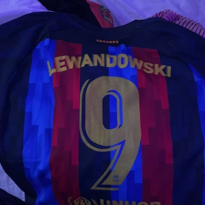 Barcelona Lewandowski tröja Nike  - Säljer en officiell FC Barcelona matchtröja med Lewandowski och nummer 9 på ryggen. Tröjan har klassiska blå och röda ränder, guldiga detaljer och sponsorloggor från Spotify. Tillverkad i lätt och ventilerande Dri-FIT material, perfekt för fotboll eller häng.