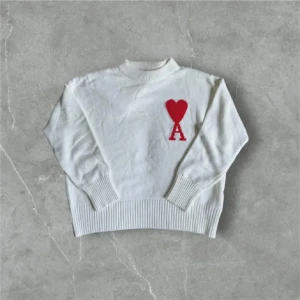 Vit stickad tröja från Ami - Vit stickad tröja från Ami Alexandre Mattiussi med röd hjärtapplikation och bokstaven A på bröstet. Tröjan har ribbad hals, muddar och nederkant samt långärmad passform. Perfekt för dig som gillar stilrena detaljer och vill ha något som sticker ut.