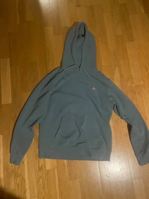 Blå hoodie från Dickies i storlek S - Säljer en blå hoodie från Dickies i storlek small. Tröjan har huva med snörning, en stor magficka och långärmade ribbade muddar. Perfekt för chill dagar och enkel att matcha med jeans eller joggers.