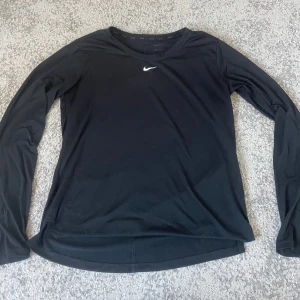 Svart långärmad Nike Dri-Fit tröja - Svart långärmad tröja från Nike. Diskret Nike-logga i vitt på bröstet och rund halsringning. 