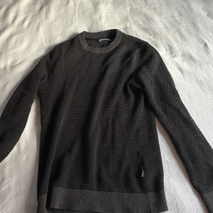 Mörkgrå stickad tröja Jack & Jones - Säljer en mörkgrå stickad tröja från Jack & Jones med diskret strukturmönster. Tröjan har rund hals, ribbade muddar vid ärmslut och nederkant samt långärmad passform. Perfekt för dig som gillar enkel och stilren look. Prisk kan diskuteras!