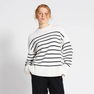 Vit och svart randig stickad tröja - Säljer en vit stickad tröja med svarta horisontella ränder. Tröjan har rund hals, långa ärmar och breda ribbade muddar vid ärmslut och nederkant. Snygg slits på sidorna ger en cool detalj. Passformen är loose, aldrig använt den 