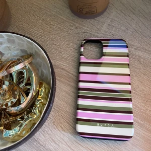 Burga Rio iPhone 12 Mobilskal - Stilrent Burga-skal till iPhone 12 i Rio-design med färgglada ränder. Dubbla lager för extra skydd: silikoninteriör och hård yttre skal. Skalet är i mycket gott skick utan synligt slitage. Perfekt för dig som vill kombinera stil och säkerhet.