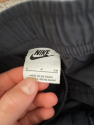 Svarta cargopants från Nike - Svarta cargopants från Nike med broderad logga på benet. Byxorna har flera fickor, elastisk midja med snörning och är tillverkade i ett slitstarkt syntetmaterial. Perfekta för en chill streetwear-look.