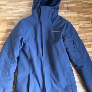 Blå Peak Performance dunjacka  - Snygg och varm Peak Performance-jacka i mörkblå färg. Mycket fint skick – inga skador eller fläckar. Vatten- och vindavvisande med vadderad insida som håller dig varm hela vintern. Stor huva, fickor fram och hög krage. OBS kan gå ner i pris vid snabbaffär