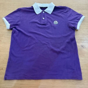 Moncler piké  - Snygg lila pikétröja från Moncler med vit krage och vita muddar på ärmarna. Bra cond