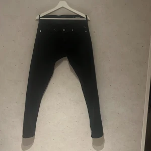 Replay Grover svarta jeans, storlek 31 - Svarta Replay Grover jeans med klassisk femficksdesign och silverfärgade detaljer. Slimmad passform med raka ben och låg midja. Jeansen är tillverkade i stretchigt bomullsmaterial för extra komfort och har diskret Replay-logga vid fickan.