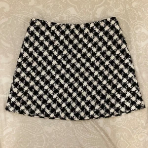 Rutig kortkjol från Zara - Säljer en snygg kortkjol från Zara med svartvitt rutigt mönster. Kjolen har en klassisk A-linjeform och är tillverkad i ett tjockare, strukturerat material som ger en cool vibe. Perfekt för dig som gillar statement-plagg och vill sticka ut.