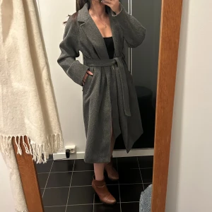 Mörkgrå Kappa - Super fin mörkgrå kappa från Gina tricot. Passar perfekt till kallare dagar!! ❄️✨ Kappan har både fickor och band runt midjan.