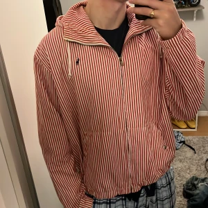 Randig vindjacka från Polo Ralph Lauren - Säljer en sjukt snygg vintage jacka/overshirt från Polo Ralph Lauren i röd och vit randigt. Jackan har huva med snörning, dragkedja framtill. Perfekt för dig som gillar klassisk streetstil. Skriv om du har några frågor, priset kan såklart diskuteras