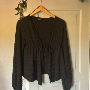 Svart blus/kofta från Gina  - Svart blus/kofta från Gina Tricot med lång ärm och knyt framtill. Blusen har en vågig, strukturerad yta och djup v-ringning. Helt utan tecken på användning❣️❣️