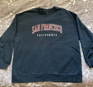 Marinblå sweatshirt med tryck - Svart sweatshirt från BikBok i storlek L med stort tryck 'San Francisco California' i rött och vitt på bröstet. (Stor i storlek)
