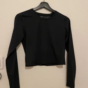 Svart långärmad träningstopp - Svart långärmad croppad topp från SOC i stretchigt syntetmaterial. Toppen har en öppen rygg med meshdetaljer. Säljer då den aldrig används