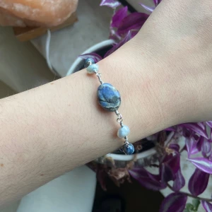 Silverarmband med stenar och pärlor i blå nyanser - Unikt armband med en stor oval blå sten i mitten och mindre blå och vita pärlor längs en tunn silverfärgad kedja. Stenarna har naturliga mönster och pärlorna ger en cool kontrast. Perfekt för dig som gillar boho eller vill sticka ut med accessoarer.