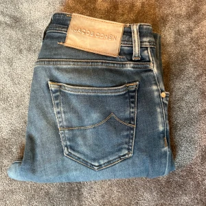 Blå jeans från Jacob Cohën - Snygga blå jeans från Jacob Cohën med slitna detaljer: Modellen är Nick Slim som sitter riktigt bra: Jeansen har ljus tvätt och är tillverkade i Italien med stretchig bomullsdenim för extra komfort: Storkek 30! Fråga mig vid minsta fundering! Nypris runt 5500!