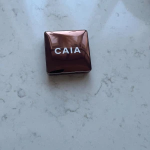 CAIA Glow Bronzer Gold Coast - Säljer en CAIA Glow Bronzer i färgen Gold Coast. Kommer i en snygg, glansig brun kompakt med spegel. Pudret har en varm, gyllenbrun ton med skimrande finish och en cirkulär, vågig yta. Perfekt för att ge ansiktet en solkysst glow.