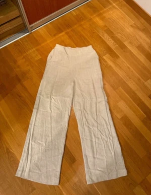 Beige linnebyxor från Kaffe, strl 38 - Snygga beige linnebyxor från Kaffe i storlek 38. Byxorna har en bred resår i midjan för extra komfort och ett loose fit med raka, vida ben. Perfekta för chill dagar och har en stilren look som funkar till sneakers eller sandaler.
