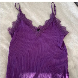 Lila spetskantad linnetopp  - Säljer en lila linnetopp i storlek M. Toppen har smala axelband, v-ringning och dekorativ spetskant längs halsringningen och ryggen💕