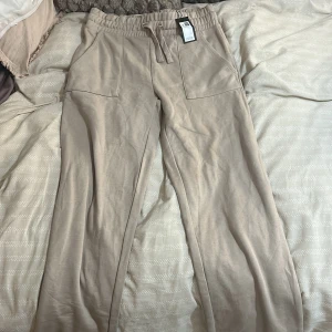 Beige mjukisbyxor med snörning från lager 157 - Säljer ett par beige mjukisbyxor från H&M med breda ben och bekväm resår i midjan. Byxorna har snörning och stora fickor framtill, perfekta för en chill och avslappnad stil. Materialet är mjukt och skönt, passar dig som gillar loose fit.