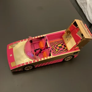 Barbie Dream Car - Färgglad Barbie-bil i rosa och guld med två säten, öppningsbart bagageutrymme och speglar. Snygg design med rutigt golv och detaljerade säten. Passar perfekt till Barbie-dockor. Mycket fint skick, inga synliga skador eller slitage.