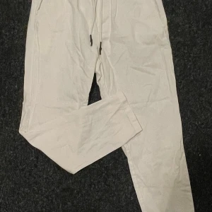 Vita tapered croppade byxor Only & Sons - Fräscha vita byxor från Only & Sons, modell Linus. De har tapered passform och är croppade i benen. Byxorna har snörning i midjan och är tillverkade i ett lätt bomullsmaterial som känns skönt mot huden. Perfekt för dig som gillar stilrena och bekväma plagg.