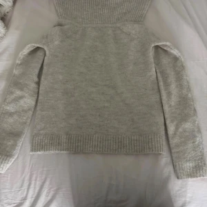 Ljusgrå off shoulder tröja  från Gina Tricot - Mysig ljusgrå polotröja från Gina Tricot med ribbade detaljer vid krage, ärmslut och nederkant. Tröjan är stickad och har lång ärm, perfekt för kyliga dagar. Enkel att matcha med jeans eller kjol för en chill look. I storlek 158