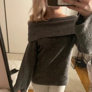 Mörkgrå offshoulder stickad tröja - Säljer en supermysig mörkgrå stickad tröja med bred offshoulder-krage. Tröjan har långa, lite vidare ärmar och är perfekt för kyliga dagar. Den stickade strukturen ger en avslappnad och trendig look.