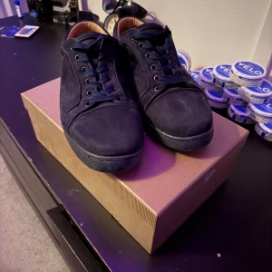 mörk blåa sneakers från Christian Louboutin - Snygga mörk blåa sneakers från Christian Louboutin i mocka med klassisk röd sula. Skorna har rund tå, mörk blåa snören och diskreta sömdetaljer. Insidan är ljusbeige och sulan har den ikoniska Louboutin-signaturen. Perfekta för dig som gillar lyxiga streetwear-vibbar. tar även emot bud!