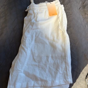 Vita linneshorts från Forever 21 - Snygga vita linneshorts från Forever 21 med elastisk midja och dragsko. Byxorna har raka ben, stora fickor framtill och är tillverkade i ett luftigt linnematerial. Perfekta för en chill och avslappnad stil.