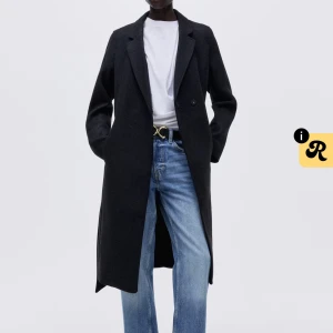 Svart kappa med bälte och slag - Stilr en svart kappa i klassisk modell med långa ärmar, breda slag och knytskärp i midjan. Kappan är rak i passformen och har en snygg längd som går nedanför knäna. Perfekt för dig som gillar minimalistisk och tidlös stil. Endast testad, nypris 599kr