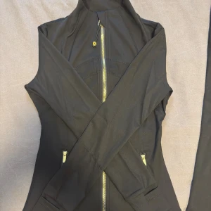 Svart set från lululemon  - Säljer ett svart set från Lululemon med stretchigt material,  Perfekta för träning eller annat. Byxorna har en diskret logga bak och tight passform med utsvängda byxben, Tröjan har guldiga detaljer med logga bak där med. Setet är helt nytt och endast testade. Vid frågor är det bara att slå en pling privat!