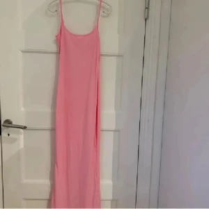 Ljusrosa långklänning med smala axelband - Säljer en enkel och stilren ljusrosa långklänning med smala axelband. Klänningen har rak passform och är ärmlös, vilket ger en clean och modern look. Perfekt för dig som gillar minimalistisk stil och mjuka färger.