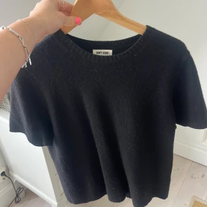 Svart kashmirtröja från Soft Goat - En svart, mjuk och lyxig kashmirtröja från Soft Goat med korta ärmar och rund hals. Tröjan har en enkel och clean design med ribbad kant vid halsen. Perfekt för dig som gillar stilrena plagg med premiumkänsla.