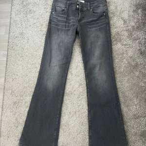 Grå bootcut jeans från Bershka - Snygga grå jeans från Bershka i bootcut-modell med klassisk femficksdesign och dragkedja. Jeansen har en mörkgrå tvätt med lätt slitning och raka ben som går ut i en lätt utsvängning. Perfekta för dig som gillar en trendig och avslappnad look.