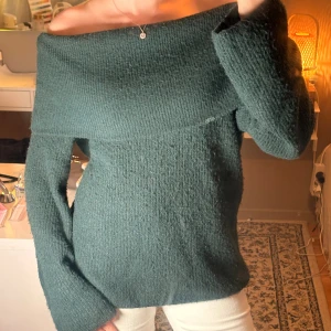 Mörkgrön stickad offshoulder-tröja - Mysig mörkgrön stickad tröja från H&M med offshoulder-design och långa ärmar. Tröjan har en bred krage som vilar snyggt över axlarna och en loose passform. Perfekt för kyliga dagar när du vill vara både bekväm och stilren.