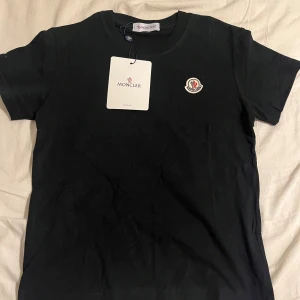 Svart Moncler t-shirt i bomull - Svart t-shirt från Moncler med klassisk rund hals och korta ärmar. T-shirten har Monclers ikoniska logga broderad på bröstet och är tillverkad i mjuk bomull. Perfekt basic med exklusiv känsla och snygg passform.