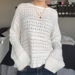 Vit stickad tröja med hålmönster - Superfin vit stickad tröja med hålmönster och breda ribbade muddar. Tröjan har en loose passform och långa ärmar, perfekt för lager på lager. Den är mjuk och har en avslappnad vibe, passar till jeans eller kjol.