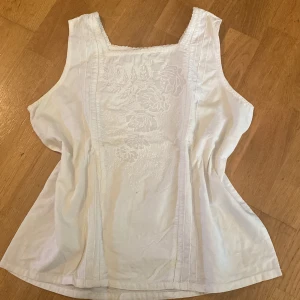Vit broderad linnetopp - Säljer en vit linnetopp med broderade blommor framtill. Toppen är ärmlös och har en lätt passform med fina sömmar längs sidorna. Toppen har en mjuk, ljus ton. Perfekt för sommarens varma dagar! Står 40 på storlekslappen men jag brukar ha 36💕
