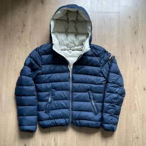 Colmar jacka - Hej, en skön, snygg och trendig dunjacka i fint skick. Marinblå utsida med beige färgad insida. Den har luva och colmar loggan sitter på vänster ärm. Stlk 42, sitter ungefär som en XS.  Hör gärna av er!