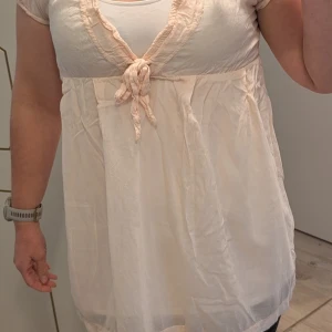 Ljusrosa kort klänning med knyt - Supersöt ljusrosa kort klänning från only med v-ringning och knyt framtill. Klänningen har korta ärmar och är tillverkad i ett tunt, luftigt material som känns perfekt för varmare dagar. Den har en lätt rynkad midja och mjuka sömmar för en avslappnad look. En liten dov fåll på fållen som inte är utmärkande vid användning.