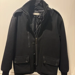 Svart bomberjacka från Stone Island - Svart bomberjacka från Stone Island med quiltat foder, hög krage i ribbstickat material och dragkedja framtill. Jackan har två stora fickor med knappar och en bröstficka med dragkedja. Klassisk och stilren design med snygga detaljer. Skulle säga att den passar folk som är 185+. Inge kvitto därav priset !