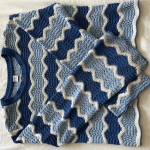 Blå stickad tröja med vågigt mönster - Superfin stickad tröja från Monki med vågigt mönster i olika blå nyanser och vitt. Tröjan har lång ärm, rund halsringning och är lite croppad. Perfekt för dig som gillar retrovibbar och vill ha något unikt i garderoben.