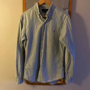 Ljusblå skjorta Polo Ralph Lauren M - Klassisk ljusblå skjorta från Polo Ralph Lauren i slim fit. Skjortan har button down-krage, broderad logga på bröstet och knäppning framtill. Tillverkad i mjuk bomull och har långa ärmar. Perfekt för en clean och stilren look. Modellen på bilderna är 183cm och väger ungefär 75kg. Pris går att diskutera