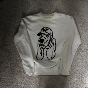 Unik vit stickad tröja🐕 - Vit stickad tröja med svart motiv av en hund med keps på framsidan. Tröjan har rund halsringning och långa ärmar. Perfekt för dig som gillar unika och lekfulla plagg. Sjukt snygg till sommaren! Bytesförslag är alltid intressant!