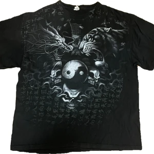 Svart t-shirt med coolt tryck - Cool svart t-shirt med stort tryck. Tröjan har två stora fläckar på ryggen. Den är XL i man storlek.