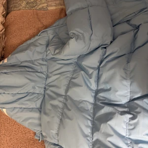 Ljusblå pufferjacka från Hoodrich S - Säljer en ljusblå pufferjacka från Hoodrich i storlek S. Jackan har huva, dragkedja framtill och sidofickor med dragkedja. Materialet är syntet och jackan är quiltad för extra värme. Perfekt för kalla dagar och har en clean streetstyle-look. Säljer eftersom att det inte är min stil längre och kommer helt enkelt inte till användning!